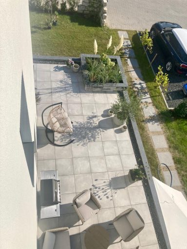 Gepflasterter Außenbereich mit Gartenmöbeln und Pflanzen, umgeben von Rasen.